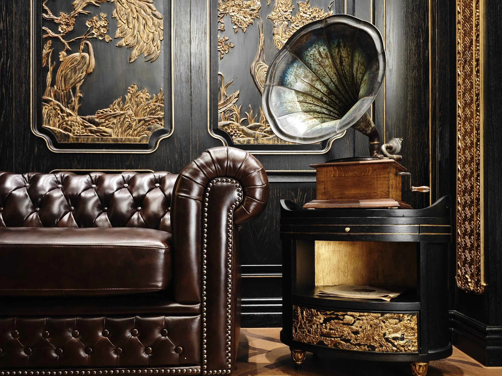 Vintage gramophone on a wooden cabinet with a brown leather sofa and decorative wall art in a room.